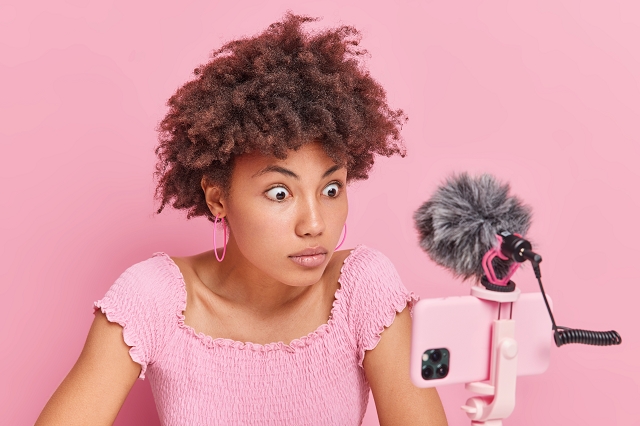 A surprised woman recording a video with a smartphone and external microphone